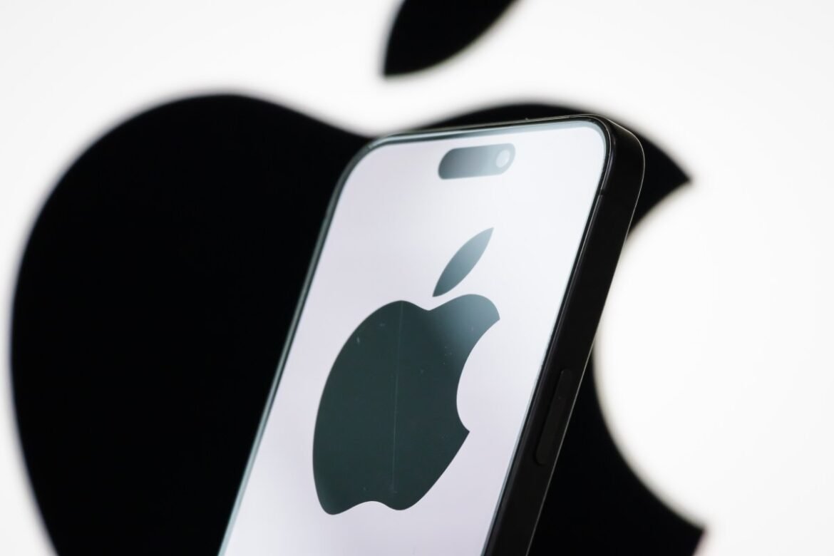 In this photo illustration, the logo of Apple Inc. is displayed on a smartphone screen, with the company's iconic black apple symbol visible in the background.