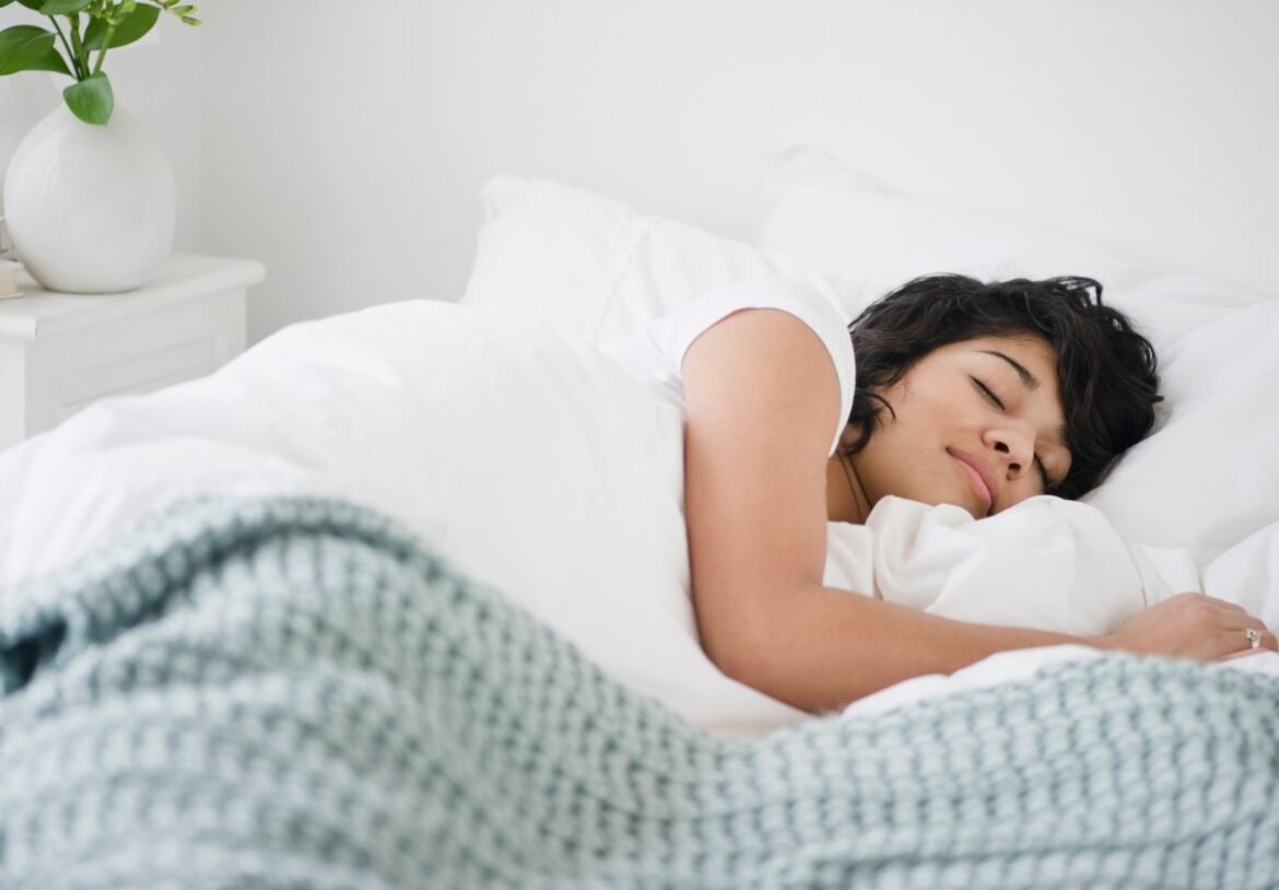 Photo of a woman sleeping in a bed with white pillows and a blue blanket