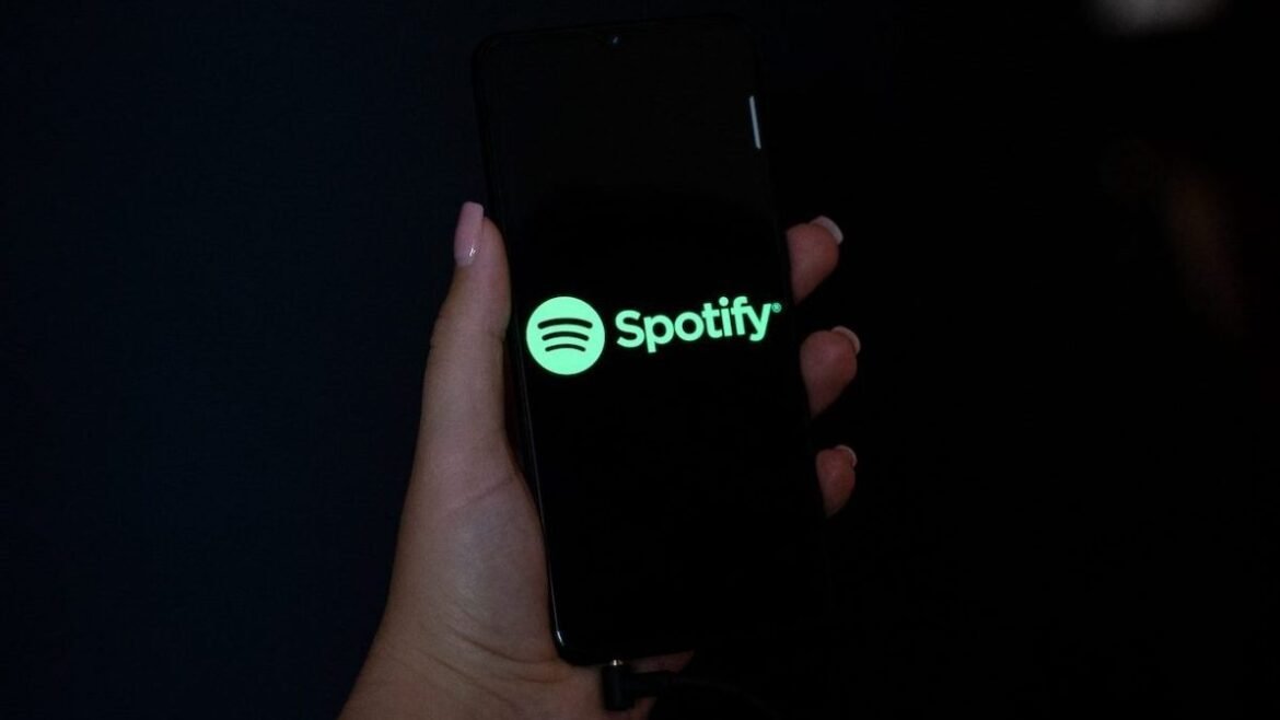 Hand holding a mobile phone with the logo of Spotify on its screen.