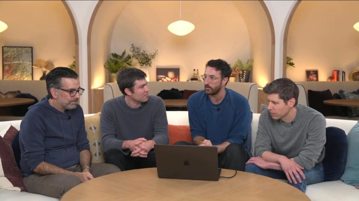 Four OpenAI employees wearing crewneck sweaters sit around a café table.