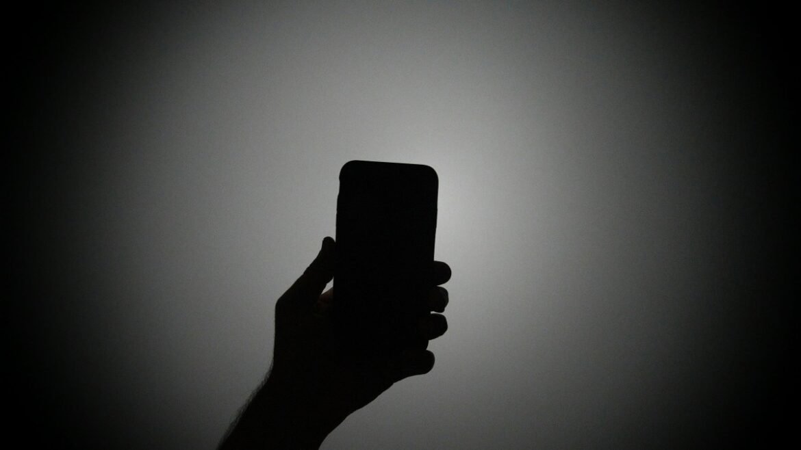 The silhouette of a hand holding an iPhone with the light on.