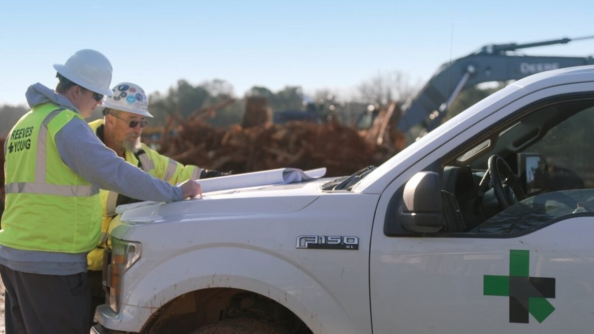 Two workmen look at plans on the hood of a Ford F150